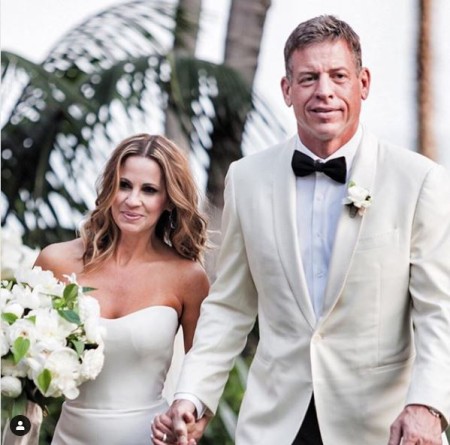 Troy Aikman and Catherine Mooty at their wedding day wearing while twining wedding dress, Bride on sleeveless white gown and groom on a white tuxedo